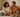 A loving couple sitting on a cozy bed, smiling and laughing together in soft morning light. Warm tones, cozy bedroom, minimalist style, intimate but wholesome atmosphere