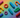 Colorful flat lay of abstract, gender-neutral silicone-like shapes on a soft rainbow pride gradient, symbolizing inclusivity and celebration.