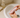 Hands washing a pastel pink silicone wellness device with soapy water in a bathroom sink, with towel and soap dispenser nearby