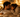 A couple cuddles closely on a bed in a softly lit room, looking relaxed, comfortable, and intimate.