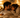 A couple cuddles closely on a bed in a softly lit room, looking relaxed, comfortable, and intimate.